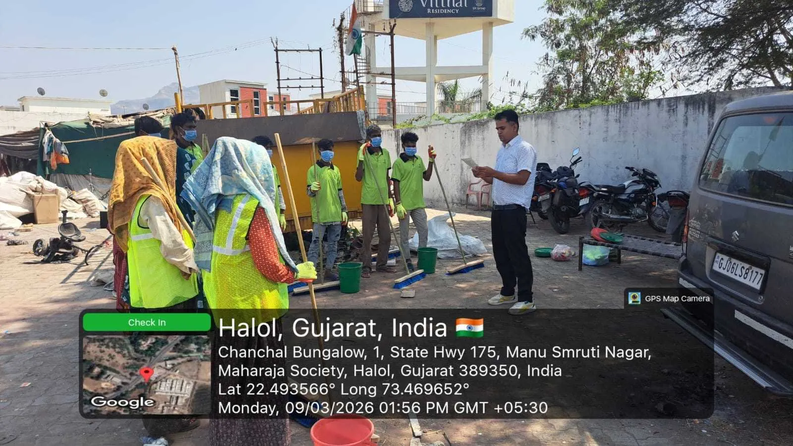 A sanitation crew in uniform, high-visibility vests and gloves standing with their brooms and buckets at a work site in Halol