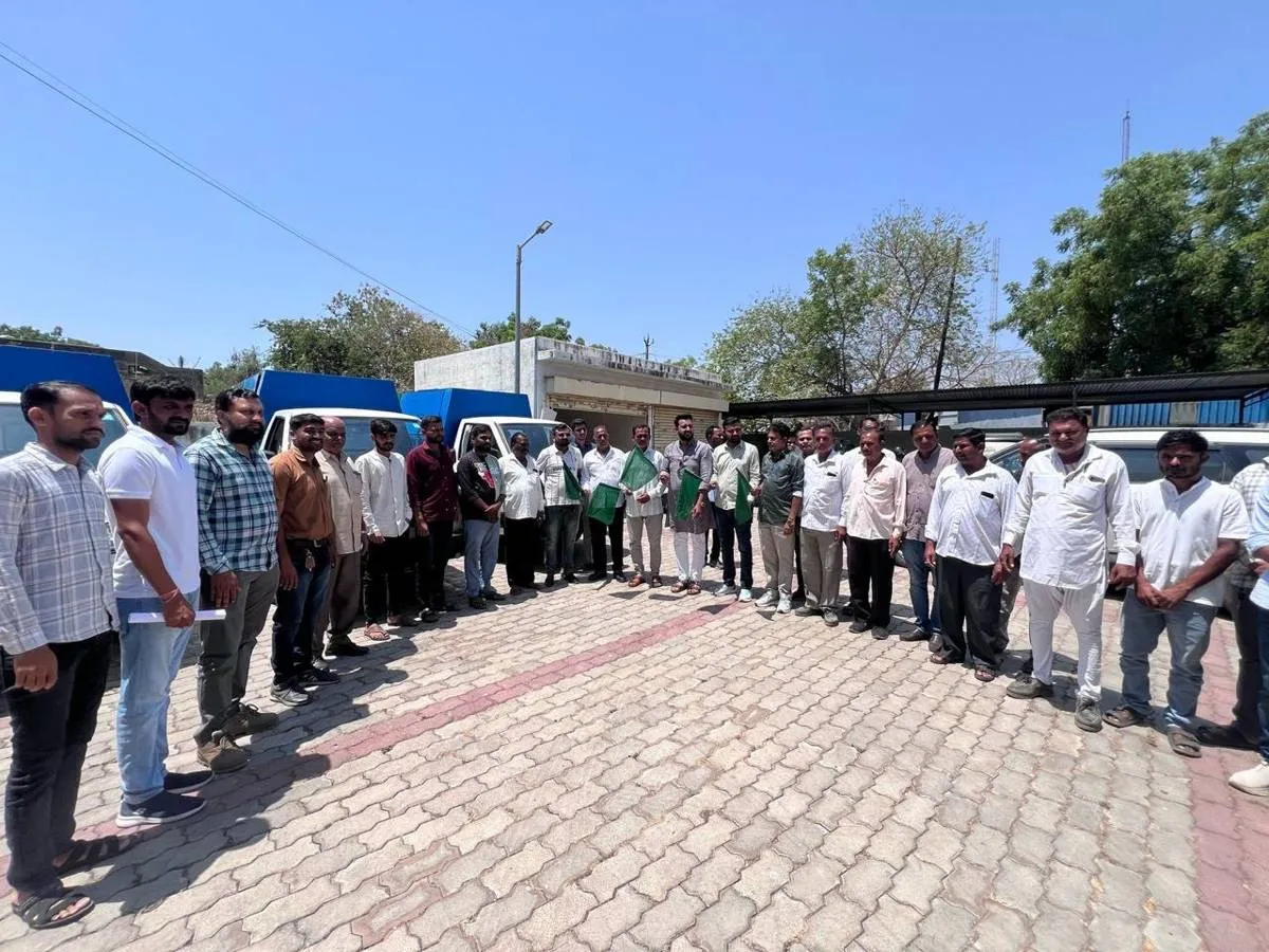 The J Kachrewala sanitation team lined up in uniform on a paved forecourt with the door-to-door collection fleet parked behind them