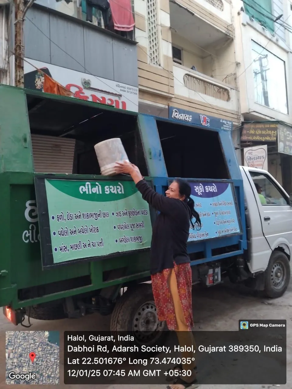 A resident tipping a household bin into the wet-waste compartment of a J Kachrewala door-to-door collection vehicle in Halol, the twin compartments signed for wet and dry waste in Gujarati
