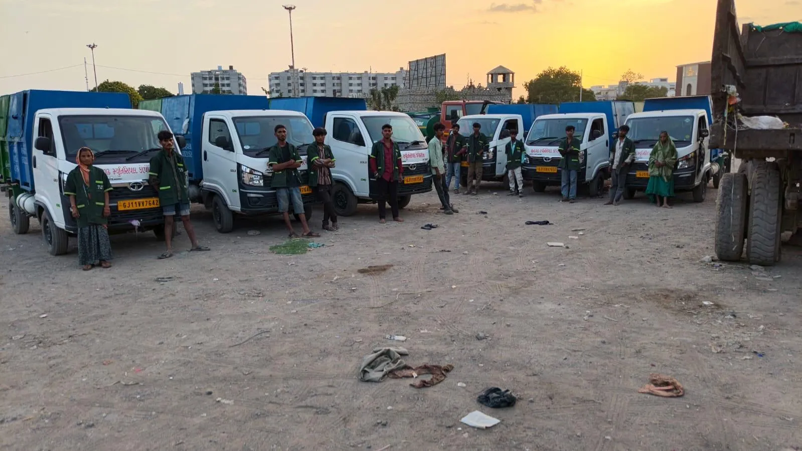 A row of door-to-door collection vehicles with their crews at the end of the shift, photographed at dusk