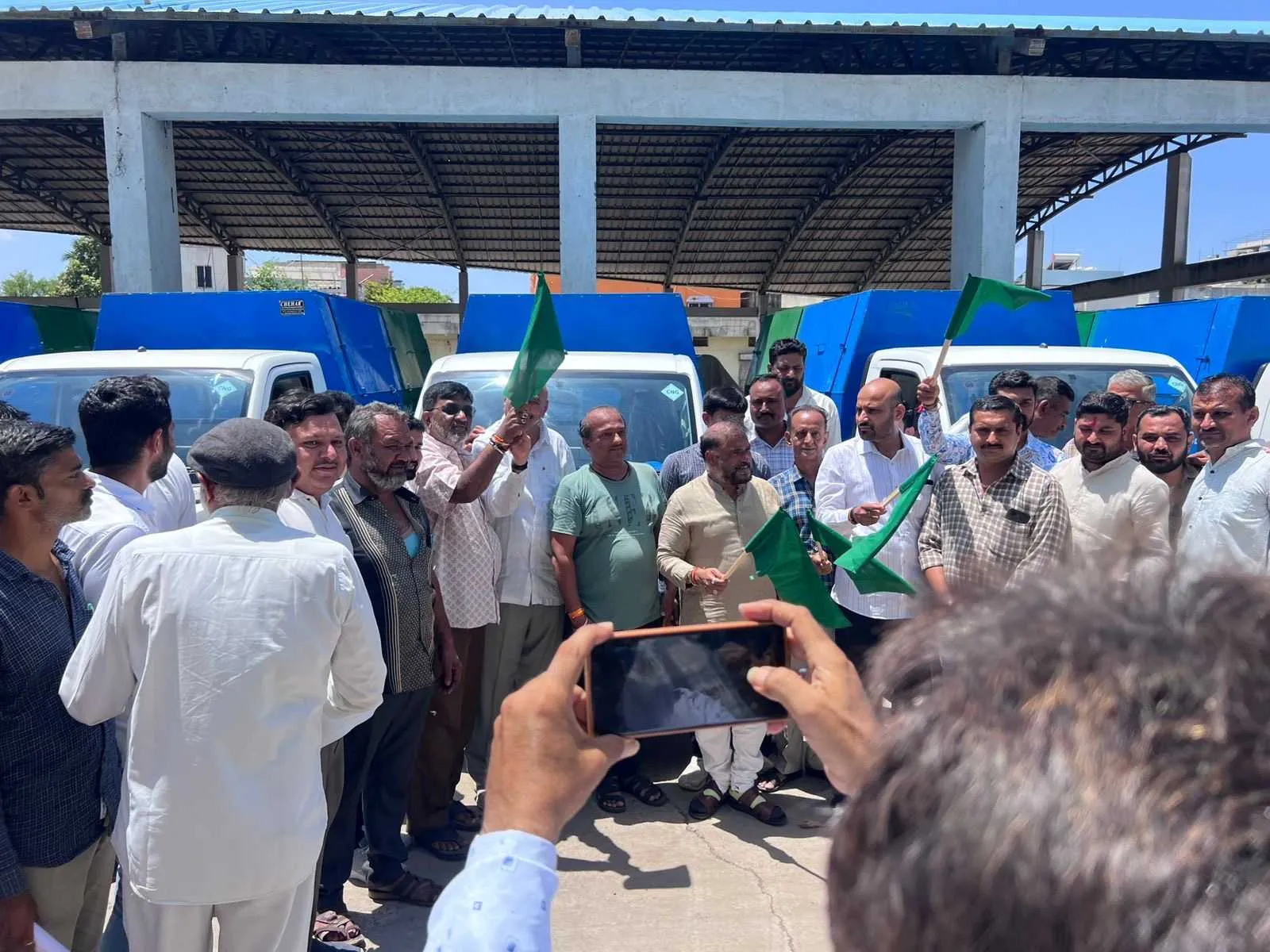 Municipal officials waving green flags to mark the flag-off of a new fleet of door-to-door collection tippers under a canopy