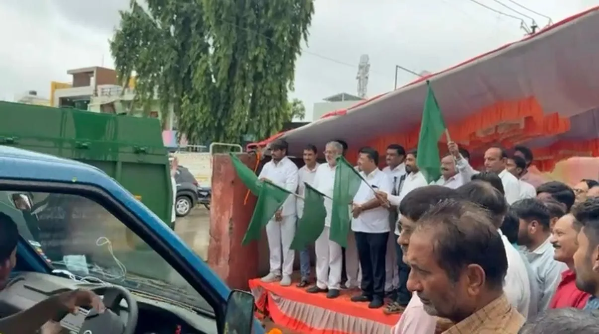 Officials and J Kachrewala staff holding green flags beside a collection vehicle at a flag-off ceremony