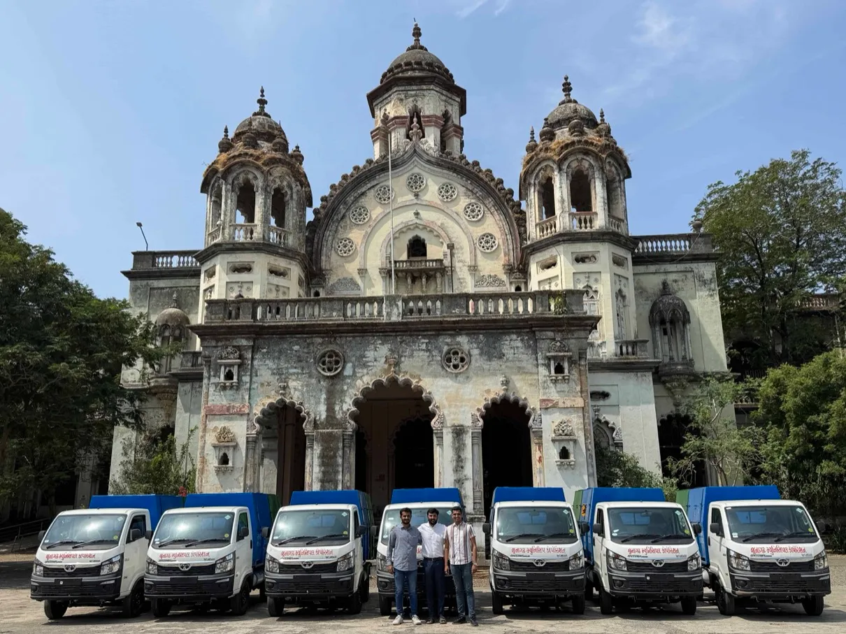 Row of Junagadh Municipal Corporation door-to-door collection vehicles operated by J Kachrewala, lined up outside a heritage municipal building