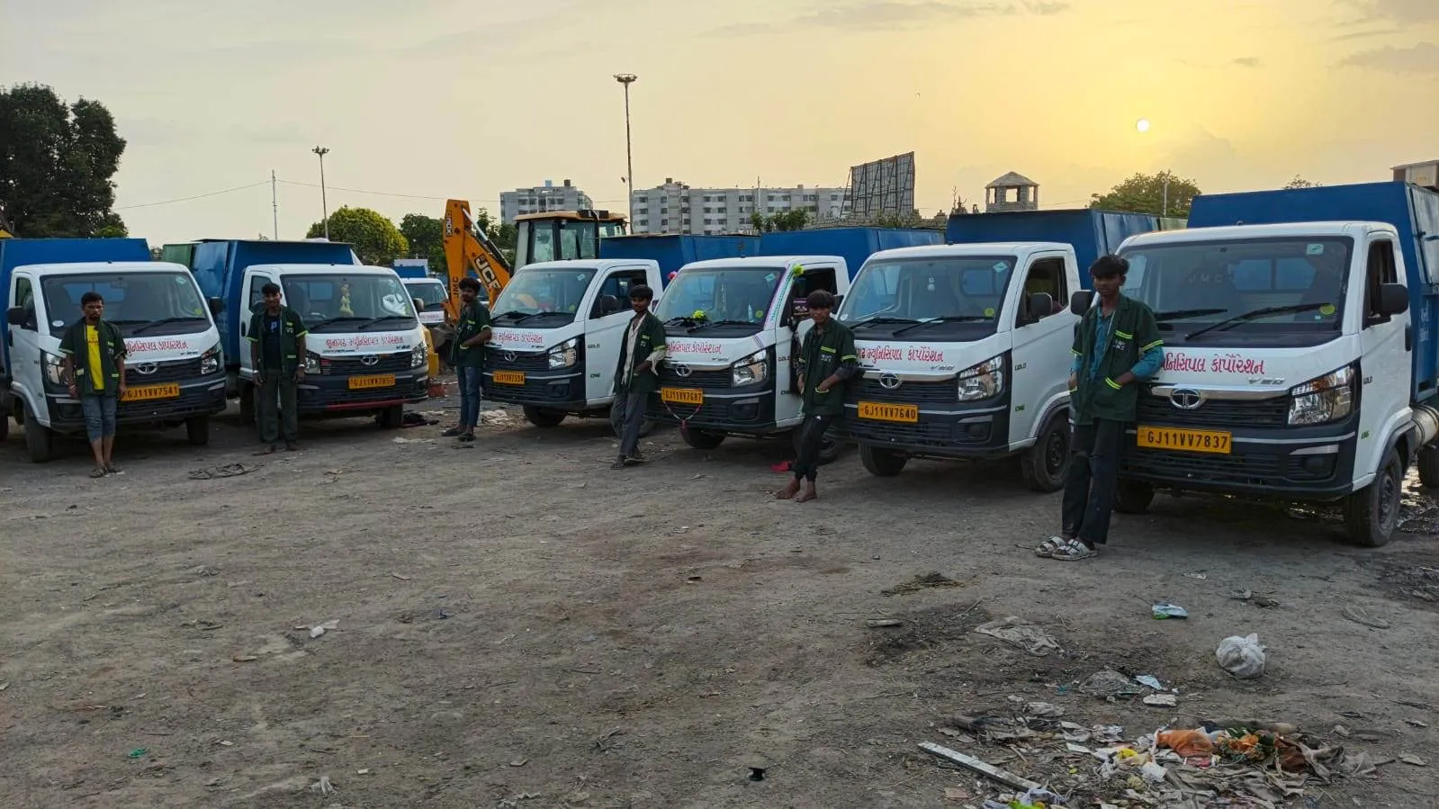 Collection vehicles and their drivers lined up across an open yard at sunset