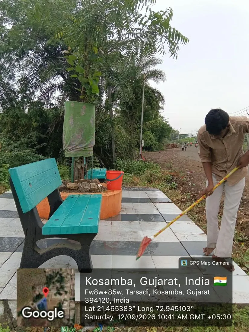 A worker sweeping a landscaped public garden with seating at Kosamba