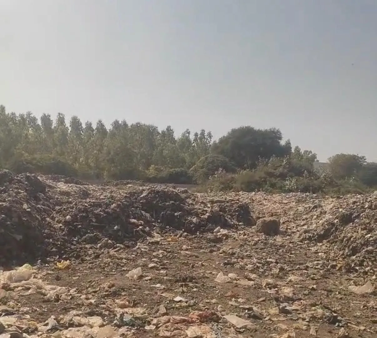 A legacy waste dumpsite before clearance, with accumulated refuse across the site