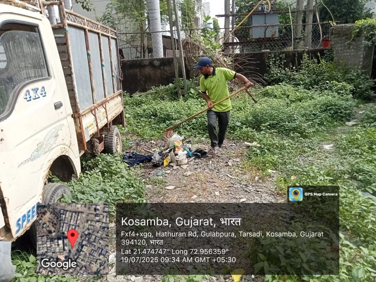 A worker clearing a scattered garbage spot beside a collection truck in Kosamba