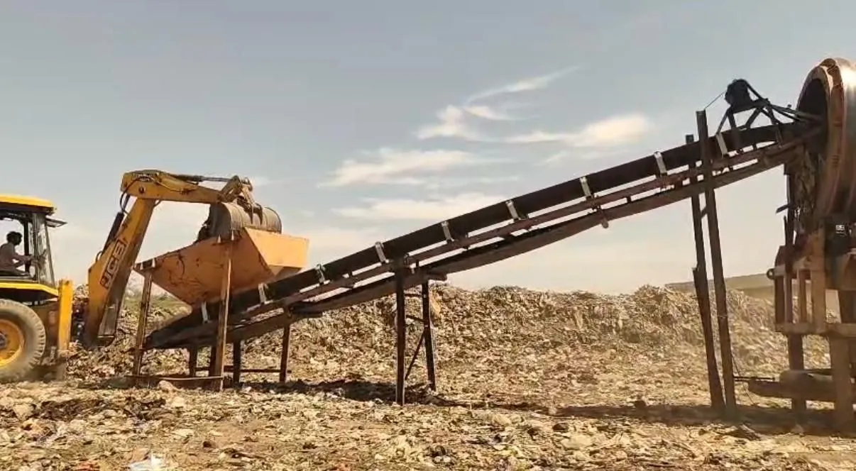 A JCB loader feeding a trommel screening conveyor during bio-remediation of a legacy waste dumpsite