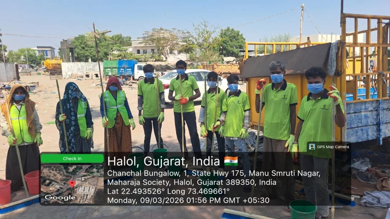 A J Kachrewala sanitation crew of nine in green uniforms, high-visibility vests, gloves and face masks standing with their brooms and buckets beside a collection tipper in Halol