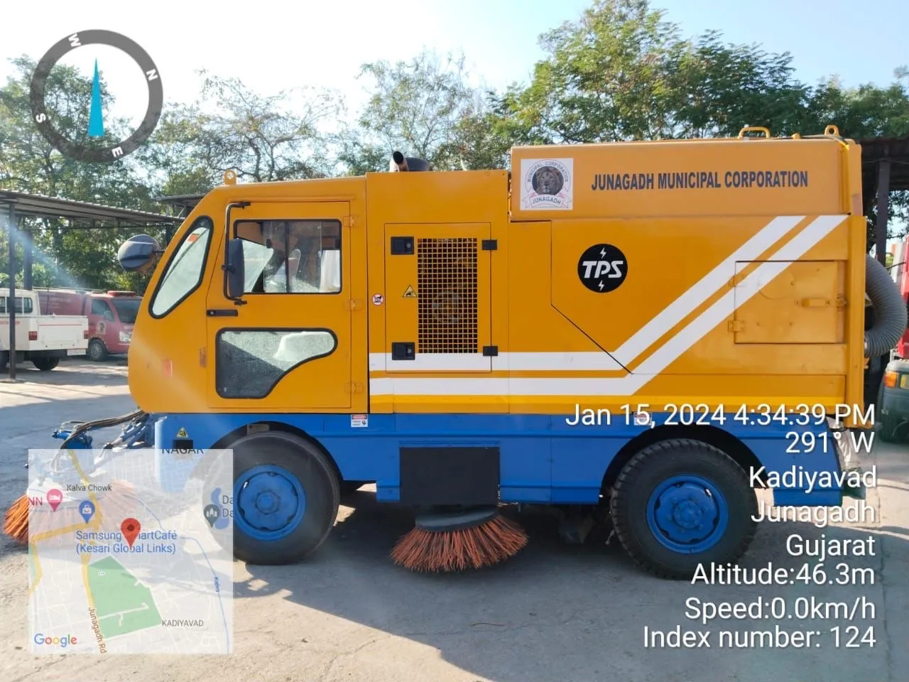 A truck-mounted mechanical road sweeper marked Junagadh Municipal Corporation, its side brooms lowered to the road, operated by J Kachrewala at Kadiyavad in Junagadh